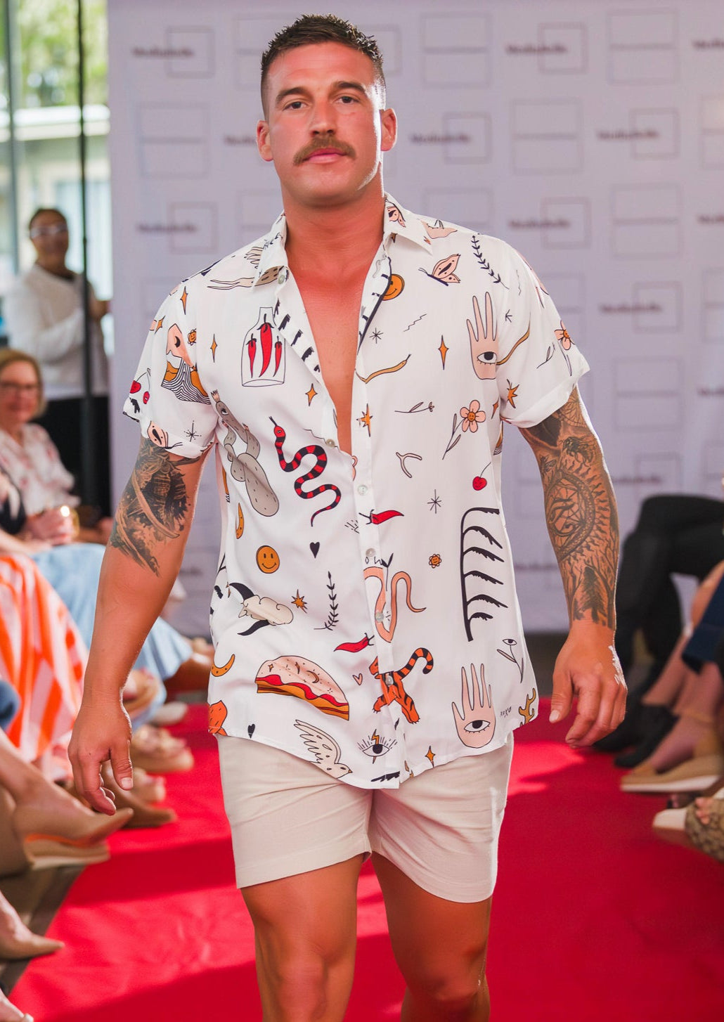 Model walking on a fashion show runway wearing our patterned greek boheme shirt and beige cotton shorts.