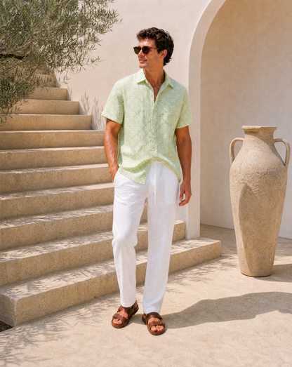 Man in light green shirt and white pants standing on stone steps with a large vase in the background.